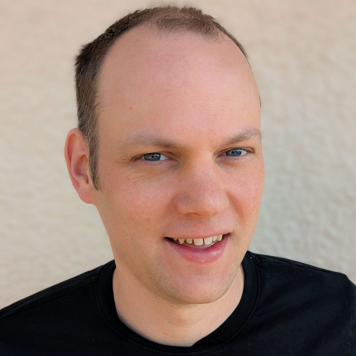 Matt Begent, smiling, wearing a black t-shirt against a pale wall.